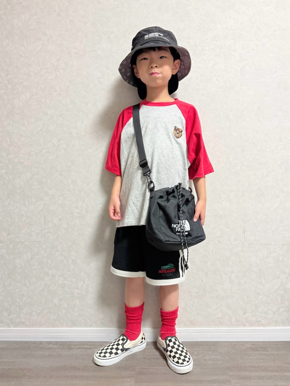 レッド系のTシャツ/カットソー、ブラック系のショルダーバッグ、ブラック系のセットアップを着用したキッズの夏コーディネートの2枚目の写真