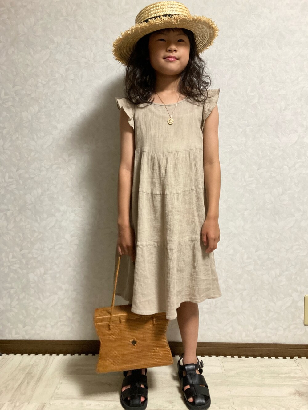 ベージュ系のワンピース、ブラウン系のかごバッグ、ブラック系のサンダルを着用したキッズの夏コーディネートの5枚目の写真