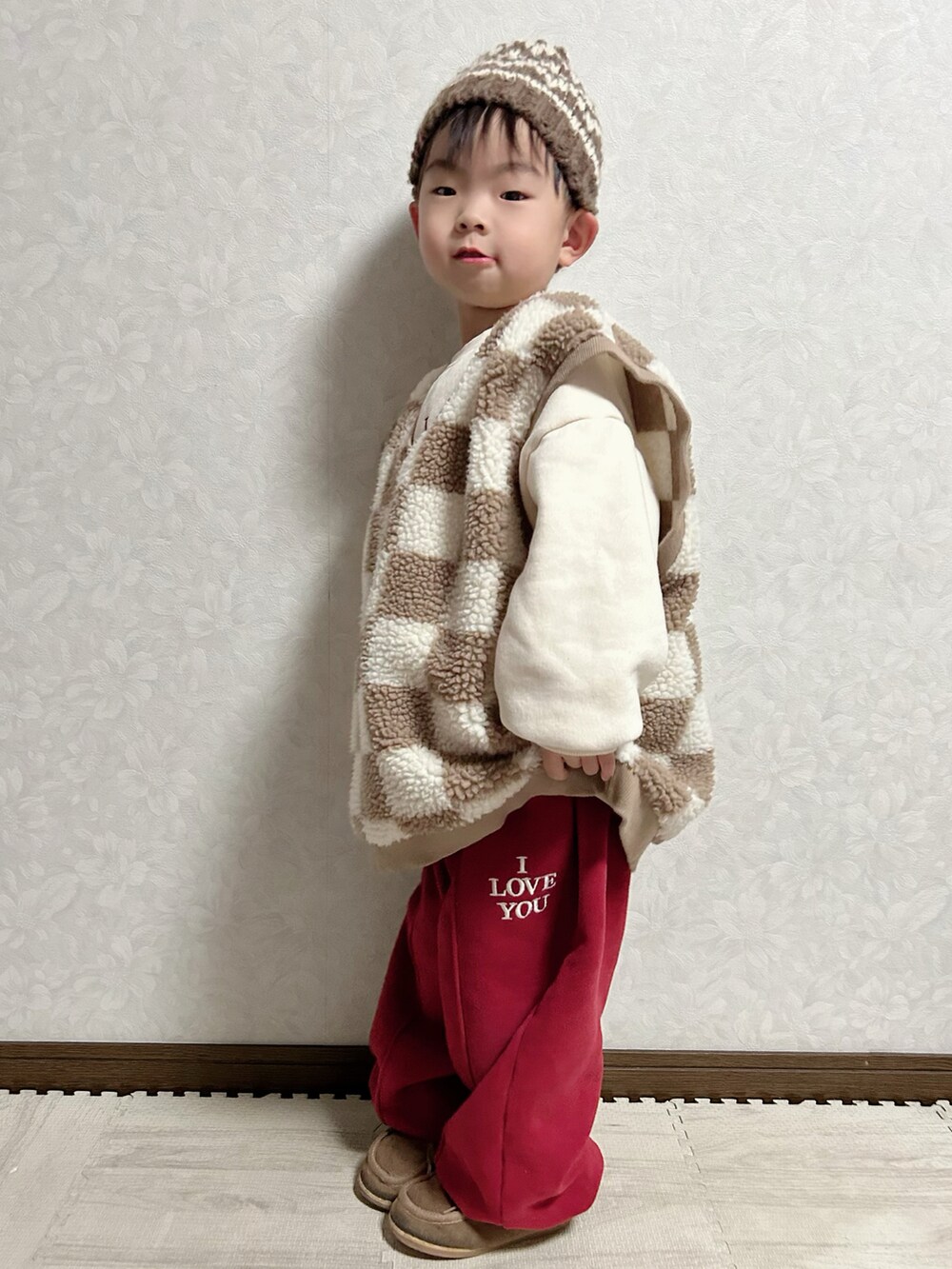 レッド系のセットアップ、ブラウン系のベスト、ベージュ系のブーツを着用したキッズの冬コーディネートの3枚目の写真