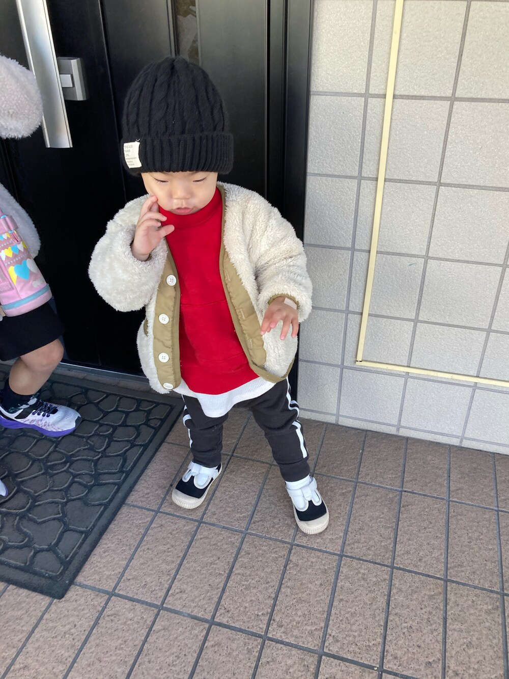 ベージュ系のノーカラージャケット、レッド系のスウェット、ブラック系のスウェットパンツを着用したキッズの冬コーディネートの3枚目の写真