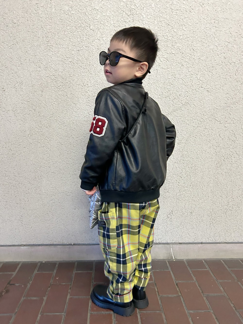 ブラック系のライダースジャケット、ホワイト系のニット/セーター、シルバー系のショルダーバッグを着用したキッズの冬コーディネートの4枚目の写真