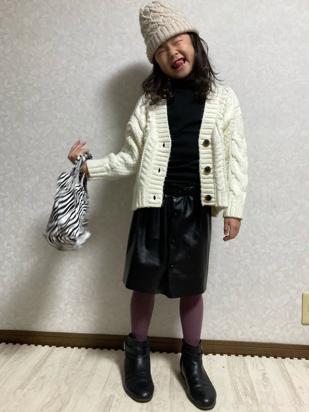 ブラック系のニット/セーター、ホワイト系のカーディガン/ボレロ、ブラック系のスカートを着用したキッズの冬コーディネートの2枚目の写真