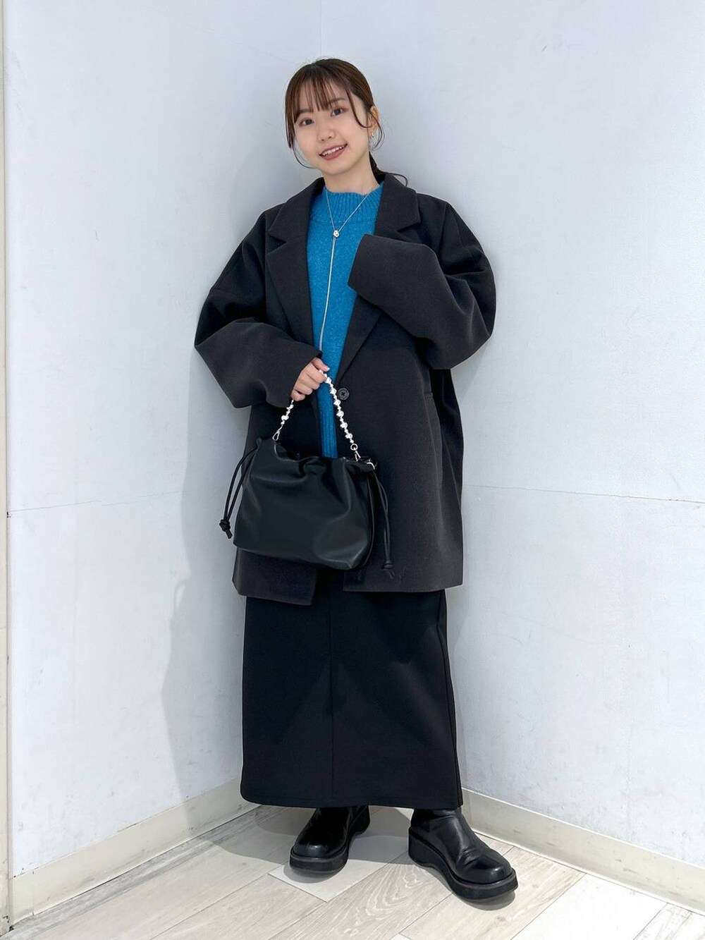 グレー系のステンカラーコート、ブラック系のブーツ、ブルー系のニット/セーターを着用したレディースの冬コーディネートの4枚目の写真