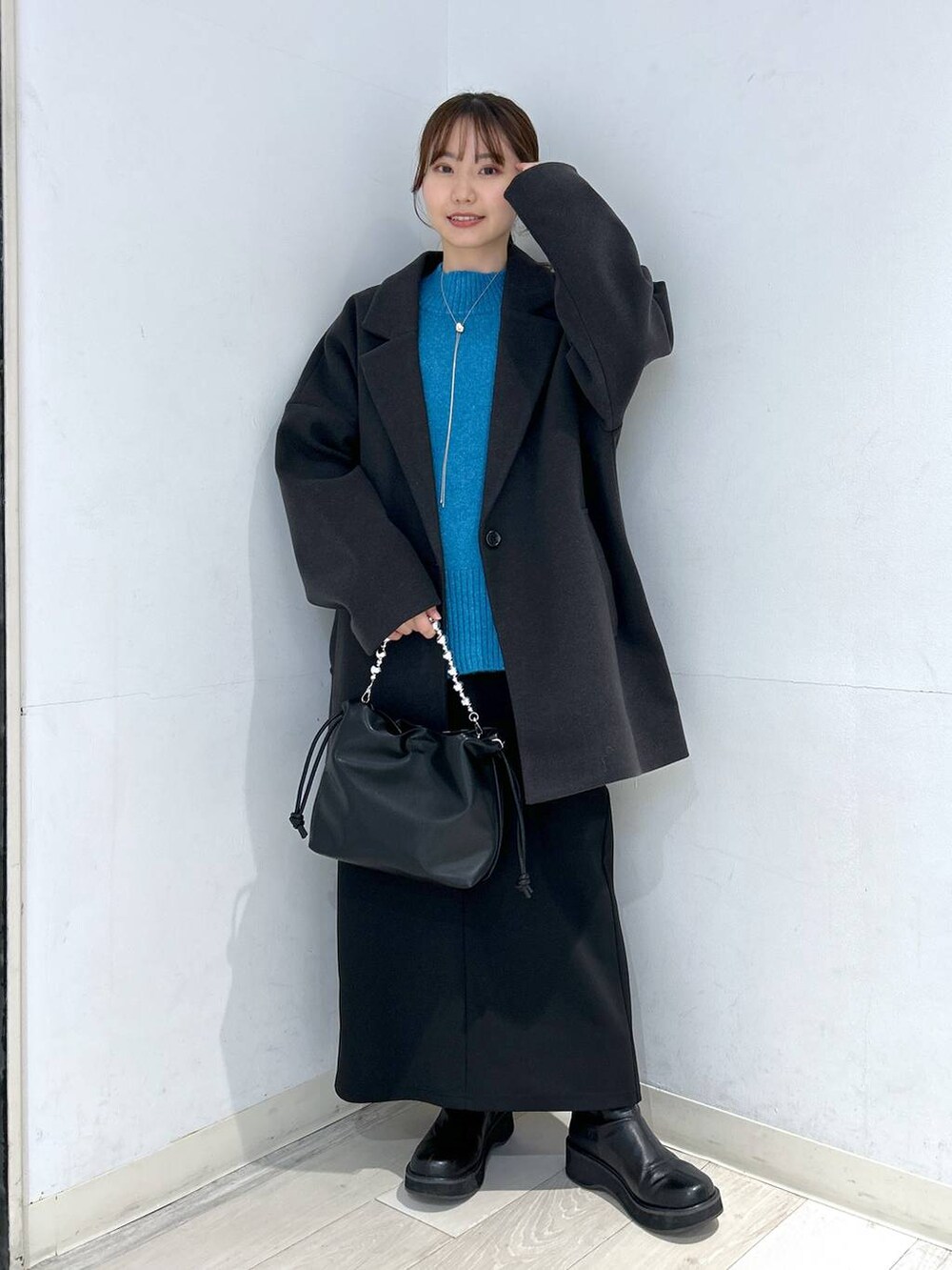 グレー系のステンカラーコート、ブラック系のブーツ、ブルー系のニット/セーターを着用したレディースの冬コーディネートの3枚目の写真