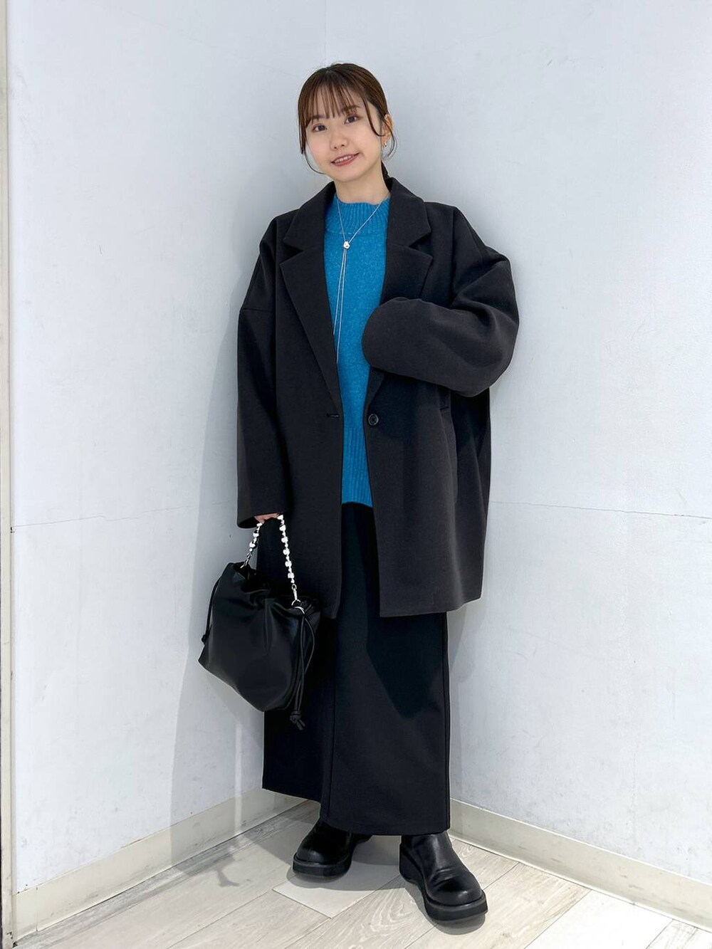 グレー系のステンカラーコート、ブラック系のブーツ、ブルー系のニット/セーターを着用したレディースの冬コーディネートの2枚目の写真