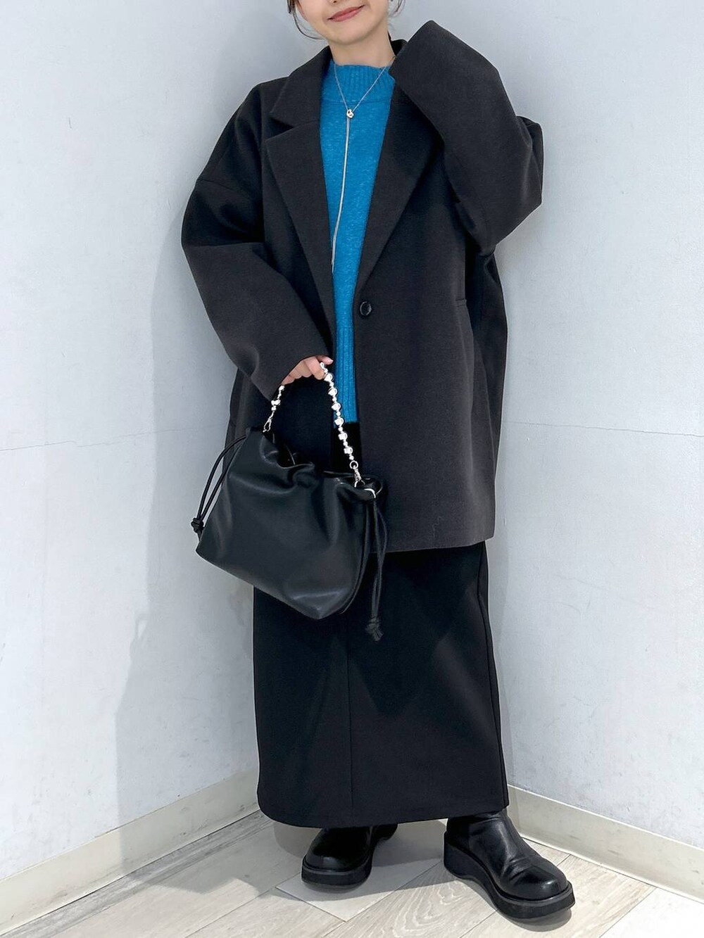 グレー系のステンカラーコート、ブラック系のブーツ、ブルー系のニット/セーターを着用したレディースの冬コーディネートの5枚目の写真