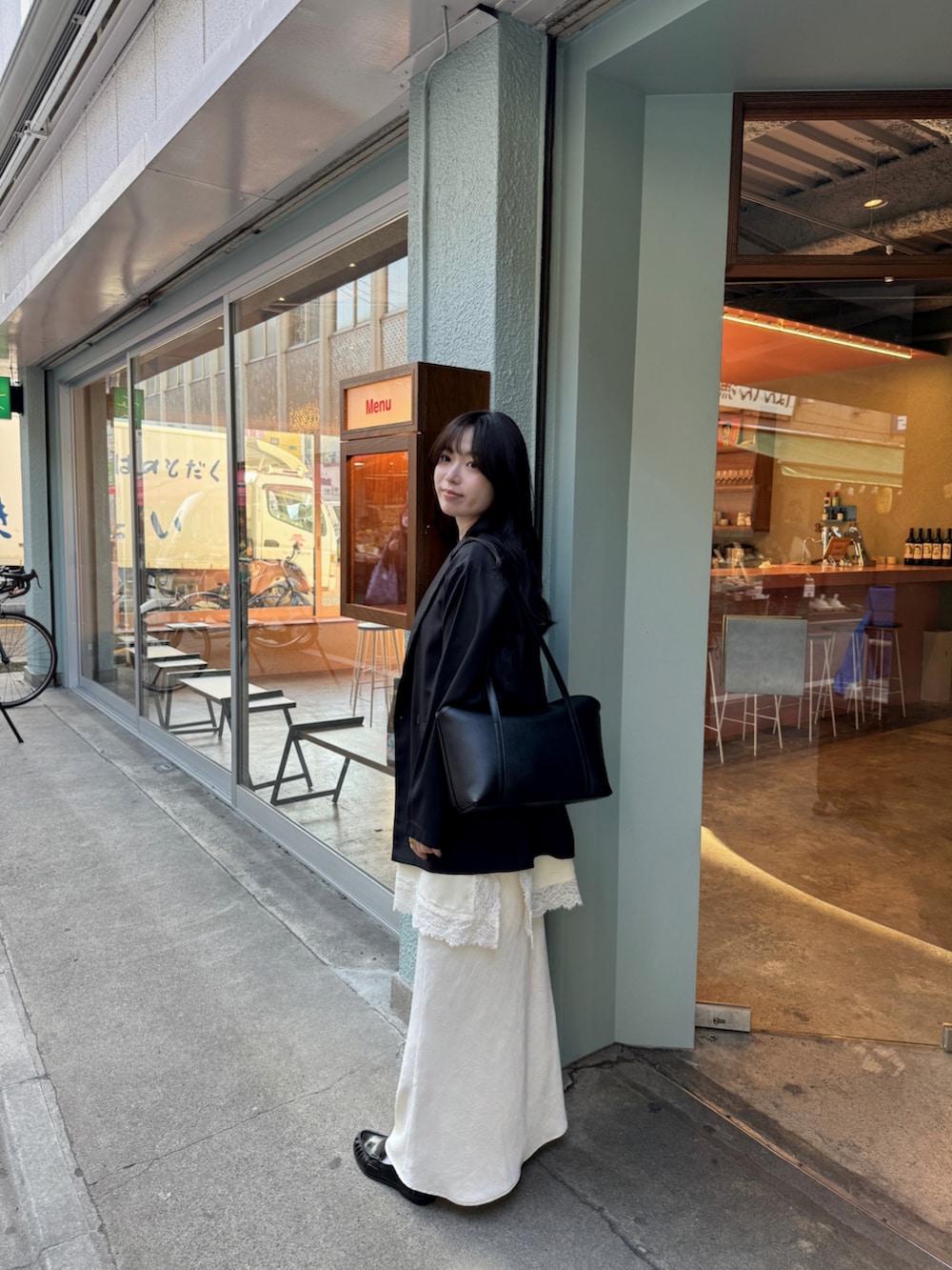 ホワイト系のスカート、ブラック系のテーラードジャケット、ブラック系のハンドバッグを着用したレディースの春コーディネートの2枚目の写真