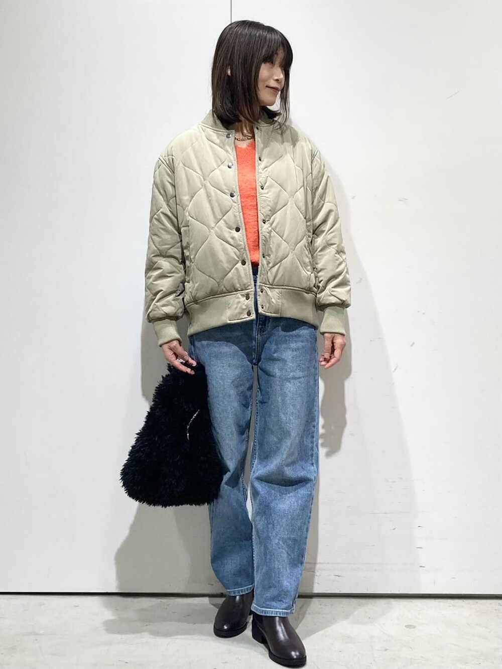 グリーン系のブルゾン、オレンジ系のニット/セーター、ブルー系のデニムパンツを着用したレディースの冬コーディネートの5枚目の写真