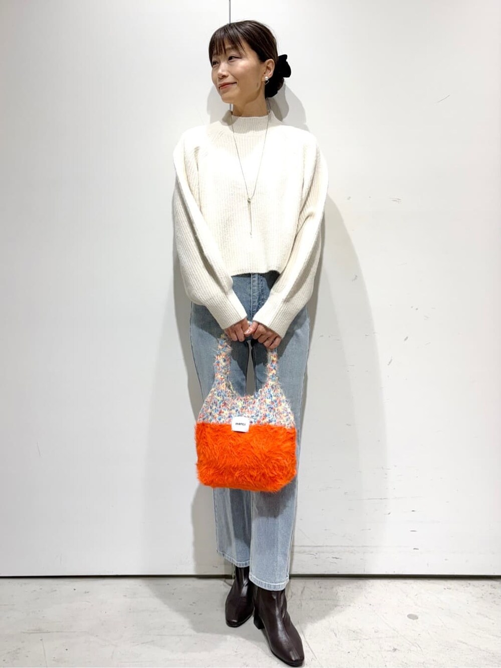 ホワイト系のニット/セーター、ブルー系のデニムパンツ、オレンジ系のトートバッグを着用したレディースの冬コーディネートの4枚目の写真