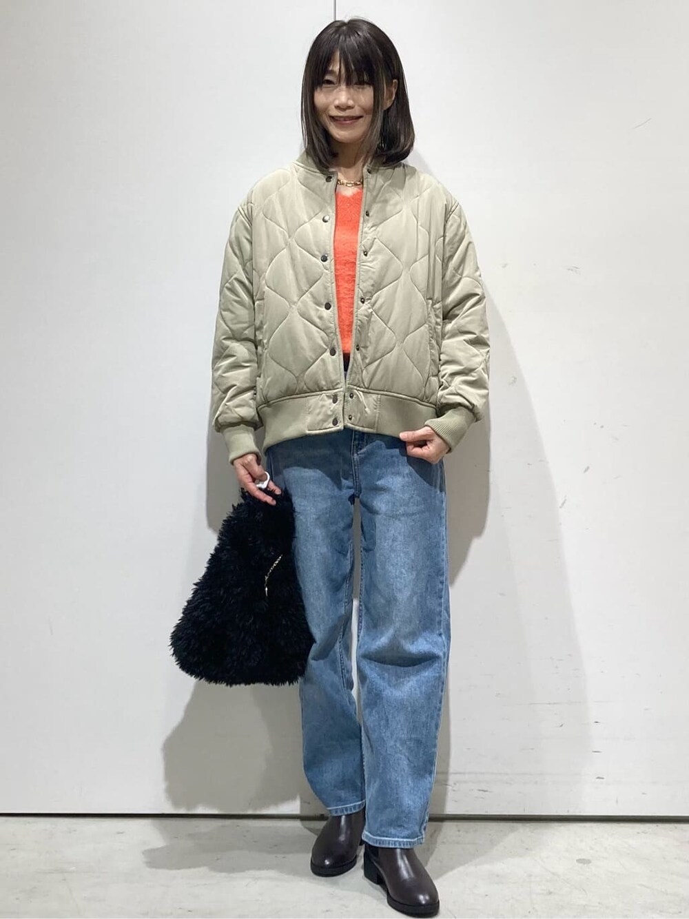 グリーン系のブルゾン、オレンジ系のニット/セーター、ブルー系のデニムパンツを着用したレディースの冬コーディネートの6枚目の写真
