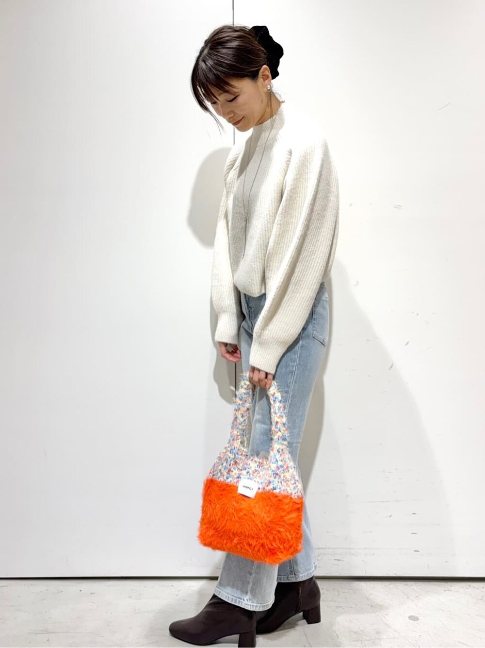 ホワイト系のニット/セーター、ブルー系のデニムパンツ、オレンジ系のトートバッグを着用したレディースの冬コーディネートの2枚目の写真