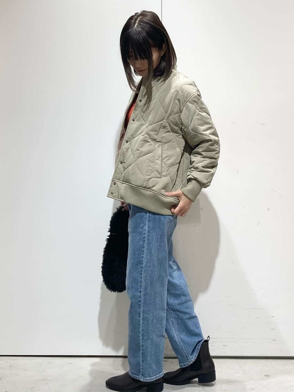 グリーン系のブルゾン、オレンジ系のニット/セーター、ブルー系のデニムパンツを着用したレディースの冬コーディネートの4枚目の写真