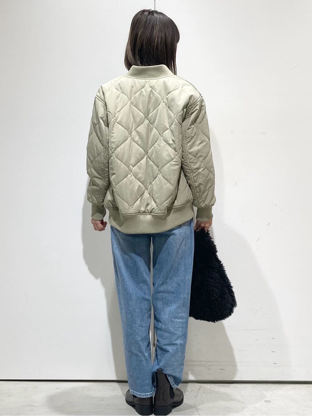 グリーン系のブルゾン、オレンジ系のニット/セーター、ブルー系のデニムパンツを着用したレディースの冬コーディネートの3枚目の写真