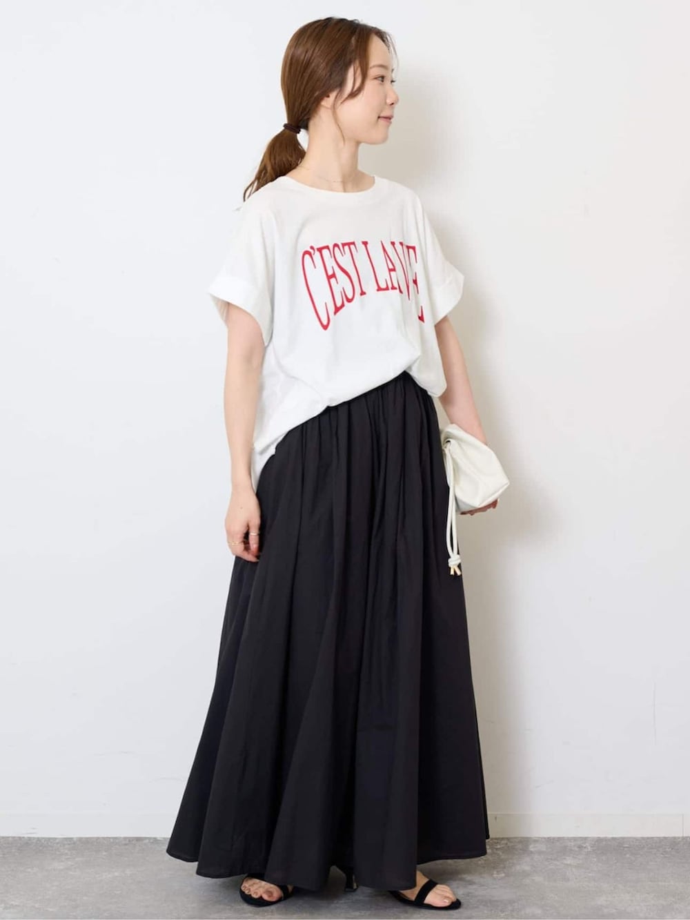 ブラック系のスカート、ホワイト系のTシャツ/カットソー、ホワイト系のクラッチバッグを着用したレディースの夏コーディネートの2枚目の写真