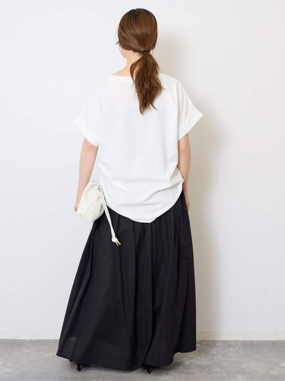 ブラック系のスカート、ホワイト系のTシャツ/カットソー、ホワイト系のクラッチバッグを着用したレディースの夏コーディネートの3枚目の写真