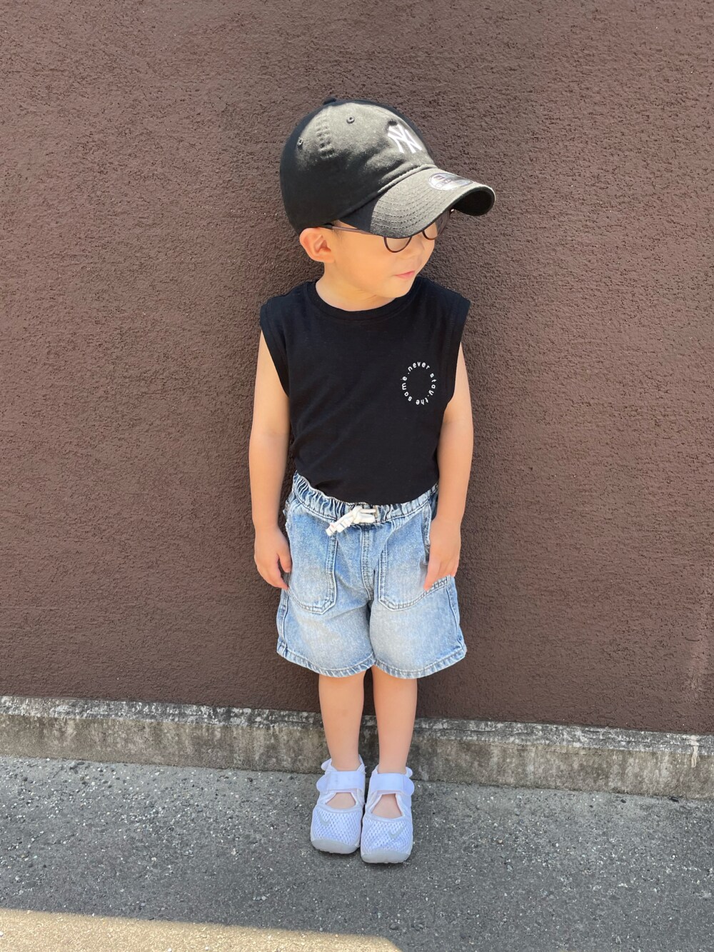 ブラック系のタンクトップ、ブルー系のデニムパンツ、ホワイト系のサンダルを着用したキッズの夏コーディネートの2枚目の写真