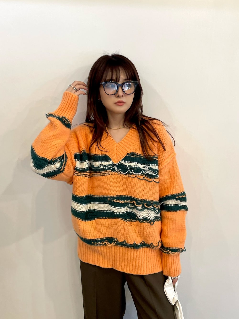 オレンジ系のニット/セーター、ブラウン系のスラックス、ホワイト系のスニーカーを着用したレディースの秋コーディネートの2枚目の写真