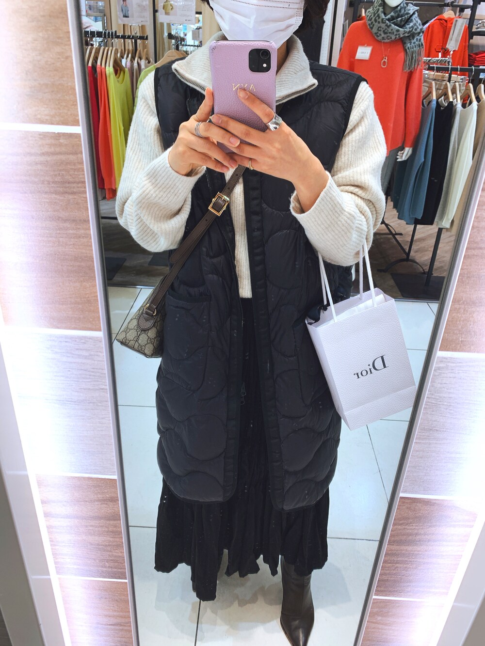 ブラック系のダウンベスト、ホワイト系のニット/セーター、ブラック系のスカートを着用したレディースの秋コーディネートの2枚目の写真