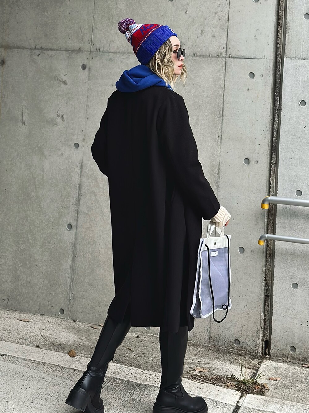 ブラック系のノーカラーコート、ブルー系のパーカー、ホワイト系のその他パンツを着用したレディースの冬コーディネートの4枚目の写真