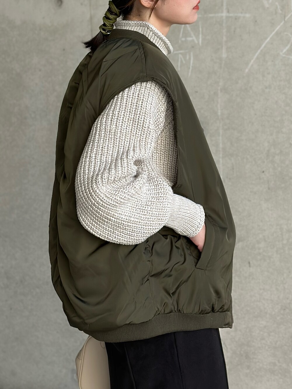 グリーン系のダウンベスト、ベージュ系のニット/セーター、ブラック系のスカートを着用したレディースの冬コーディネートの4枚目の写真