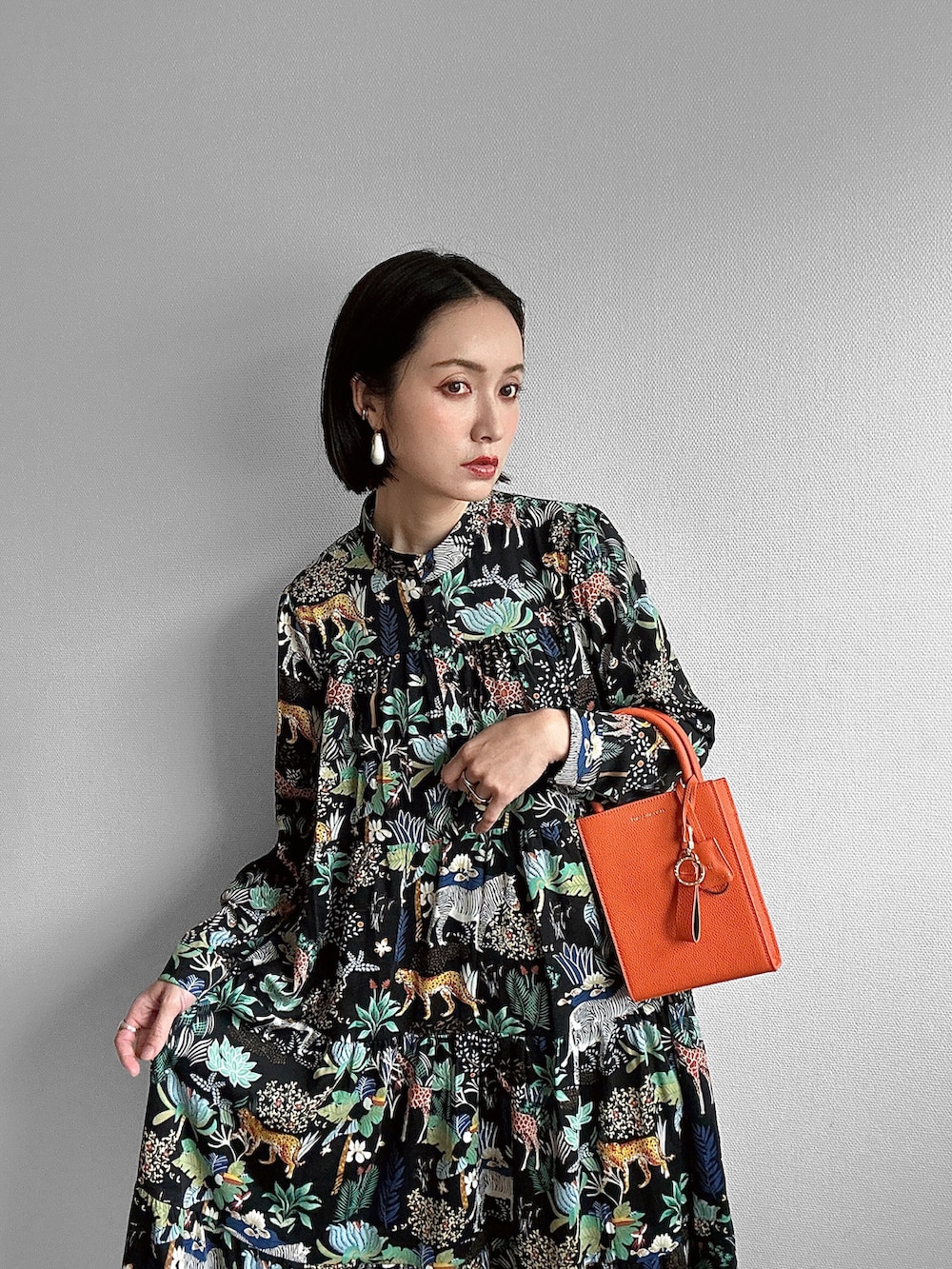 ブラック系のワンピース、シルバー系のサンダル、オレンジ系のトートバッグを着用したレディースの春コーディネートの2枚目の写真