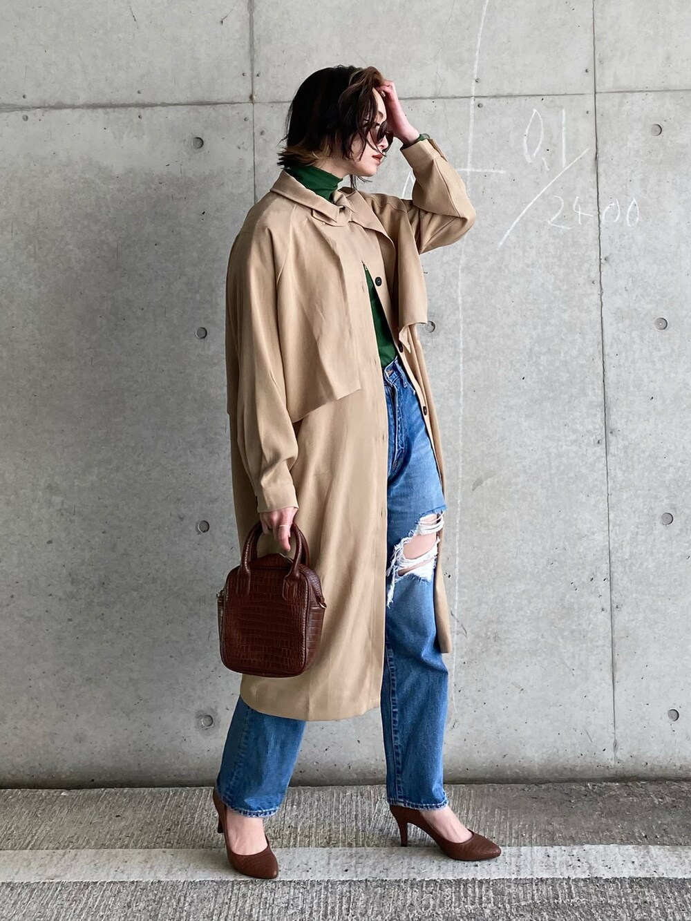 ベージュ系のトレンチコート、ブルー系のデニムパンツ、ブラウン系のハンドバッグを着用したレディースの冬コーディネートの2枚目の写真