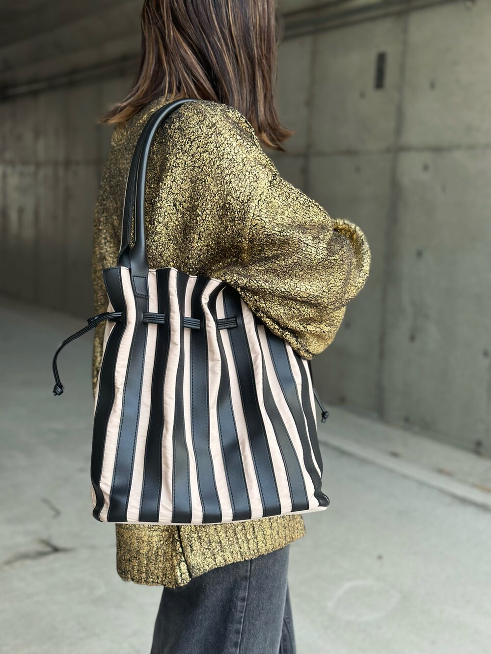 ブラック系のデニムパンツ、ゴールド系のニット/セーター、ベージュ系のトートバッグを着用したレディースの冬コーディネートの5枚目の写真