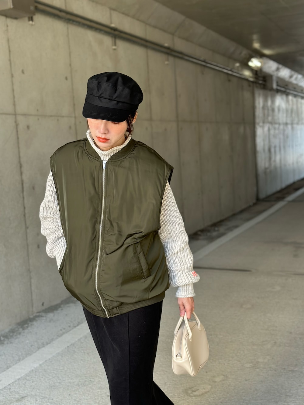 グリーン系のダウンベスト、ベージュ系のニット/セーター、ブラック系のスカートを着用したレディースの冬コーディネートの5枚目の写真