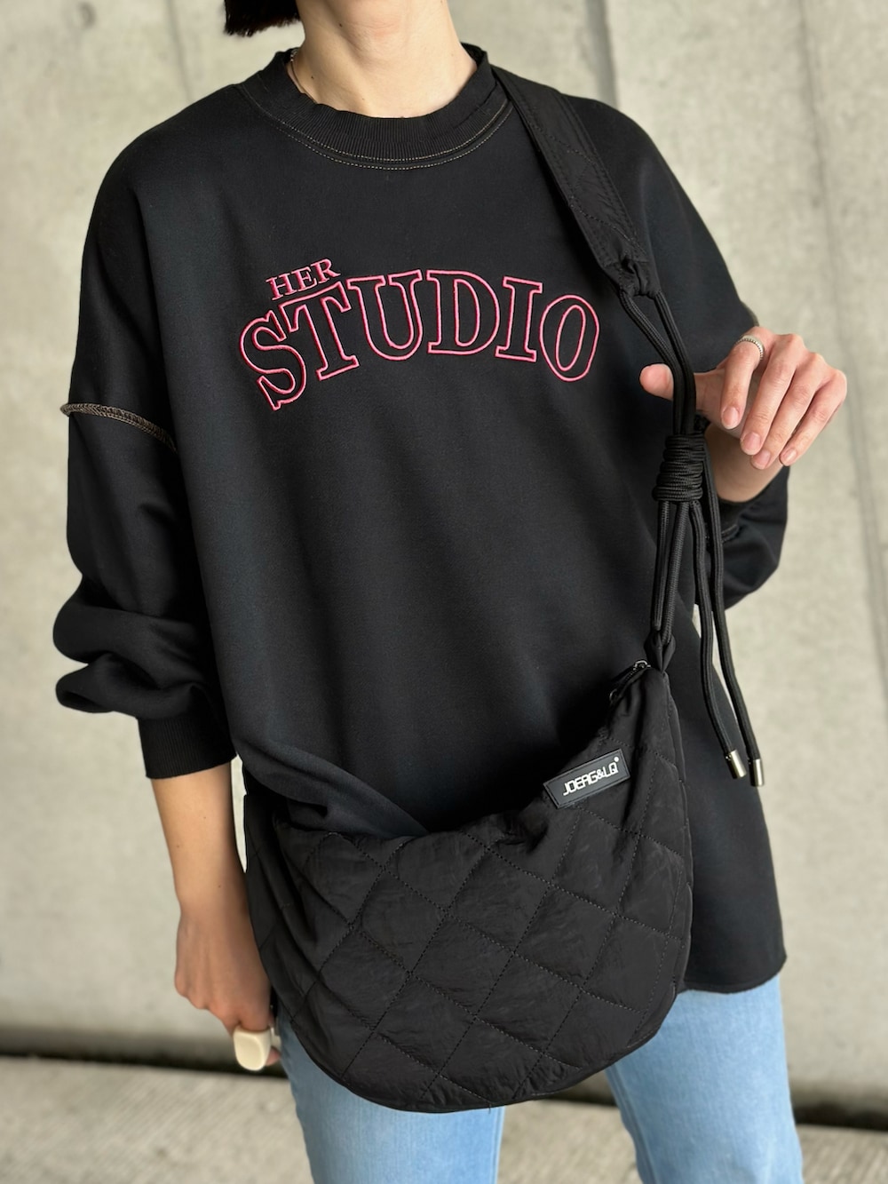 ブルー系のデニムパンツ、ブラック系のショルダーバッグ、ブラック系のスウェットを着用したレディースの春コーディネートの2枚目の写真