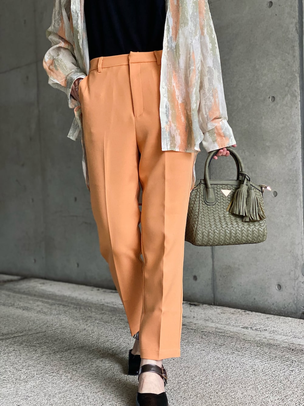 ブラック系のTシャツ/カットソー、オレンジ系のスラックス、グリーン系のハンドバッグを着用したレディースの春コーディネートの3枚目の写真