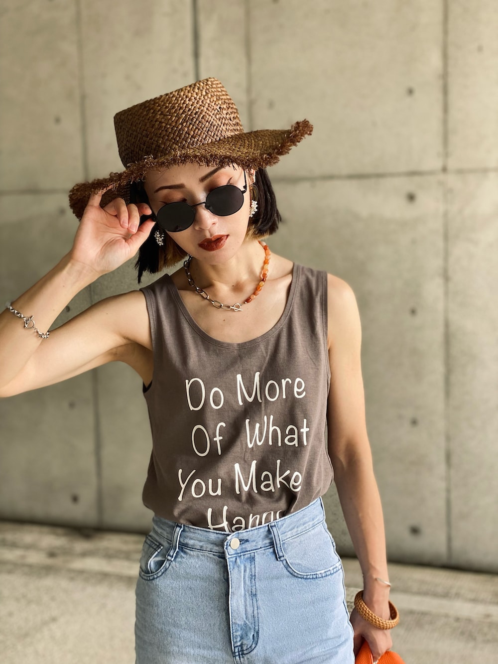 イエロー系のハンドバッグ、ホワイト系のタンクトップ、ブルー系のデニムパンツを着用したレディースの夏コーディネートの2枚目の写真