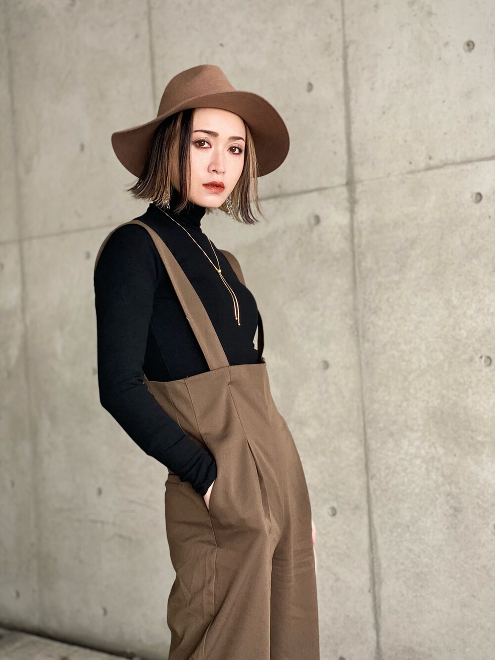 ブラウン系のサロペット/オーバーオール、ブラック系のTシャツ/カットソー、ブラック系のブーツを着用したレディースの冬コーディネートの2枚目の写真