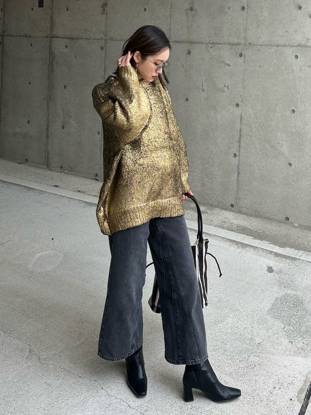 ブラック系のデニムパンツ、ゴールド系のニット/セーター、ベージュ系のトートバッグを着用したレディースの冬コーディネートの4枚目の写真