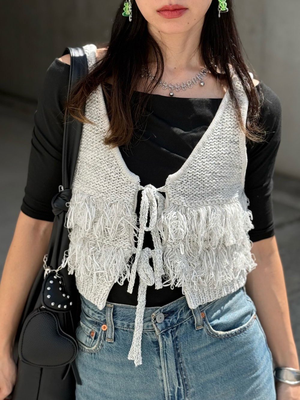 グレー系のベスト、ブラック系のトートバッグ、ブルー系のデニムパンツを着用したレディースの秋コーディネートの2枚目の写真