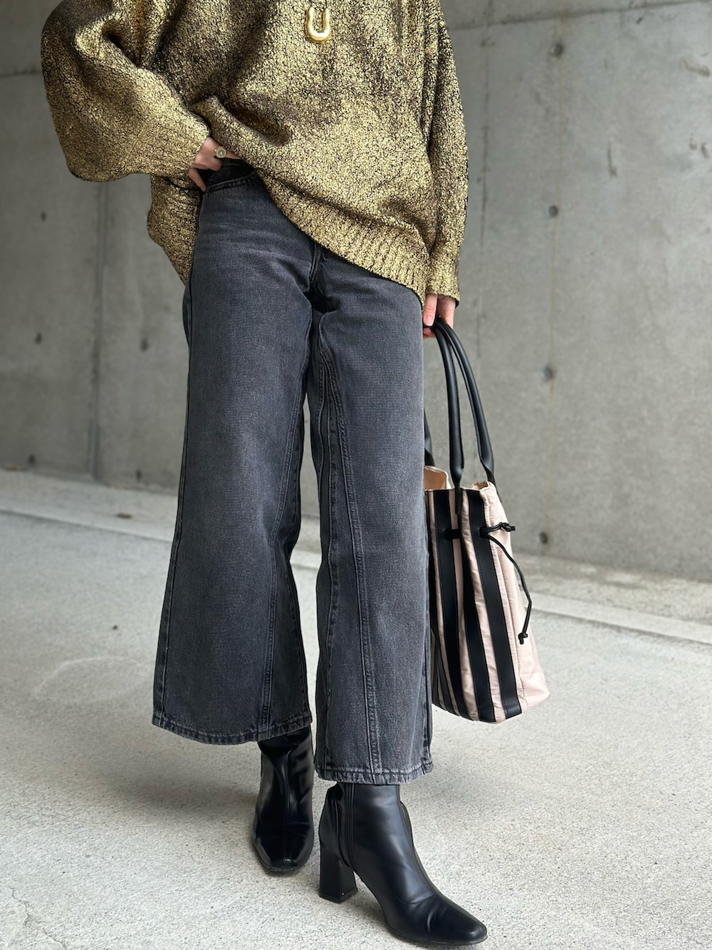 ブラック系のデニムパンツ、ゴールド系のニット/セーター、ベージュ系のトートバッグを着用したレディースの冬コーディネートの3枚目の写真