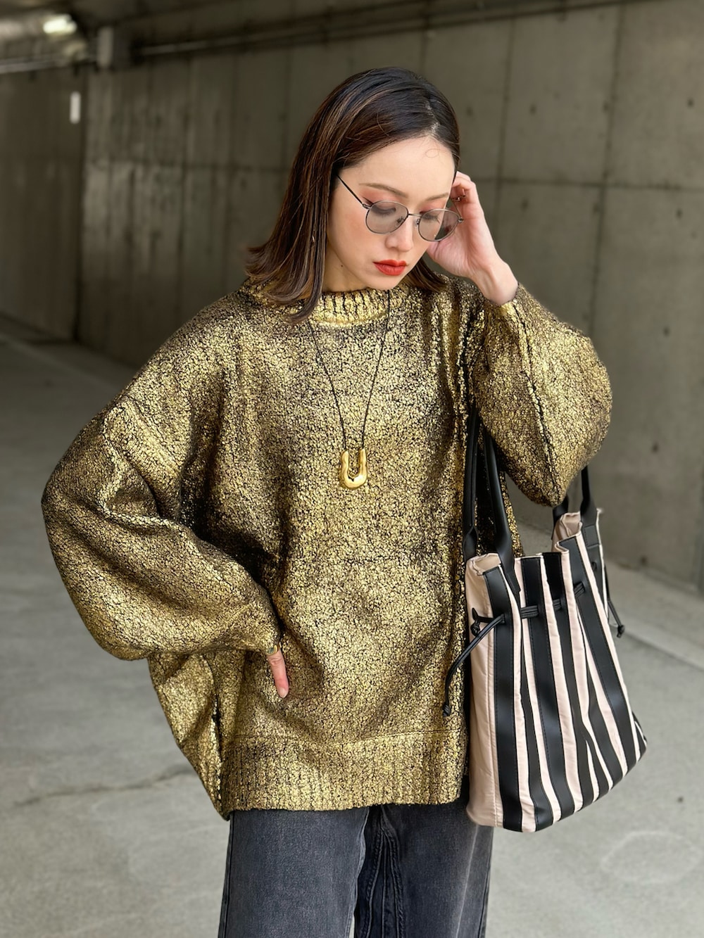 ブラック系のデニムパンツ、ゴールド系のニット/セーター、ベージュ系のトートバッグを着用したレディースの冬コーディネートの2枚目の写真