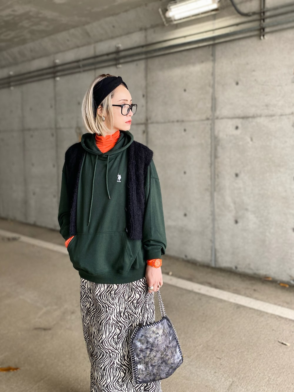 グリーン系のパーカー、ブラック系のベスト、オレンジ系のTシャツ/カットソーを着用したレディースの冬コーディネートの2枚目の写真