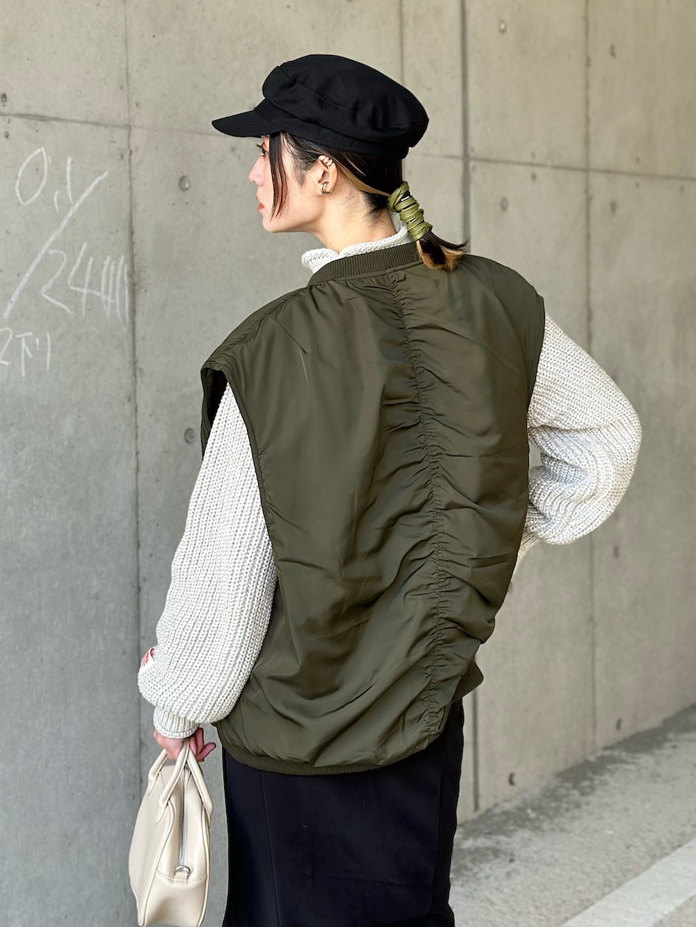 グリーン系のダウンベスト、ベージュ系のニット/セーター、ブラック系のスカートを着用したレディースの冬コーディネートの2枚目の写真