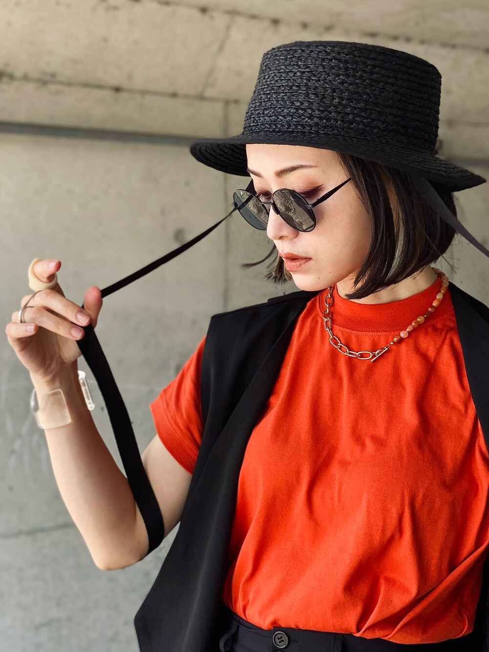 オレンジ系のTシャツ/カットソー、ブラック系のベスト、ブラック系のハンドバッグを着用したレディースの夏コーディネートの5枚目の写真