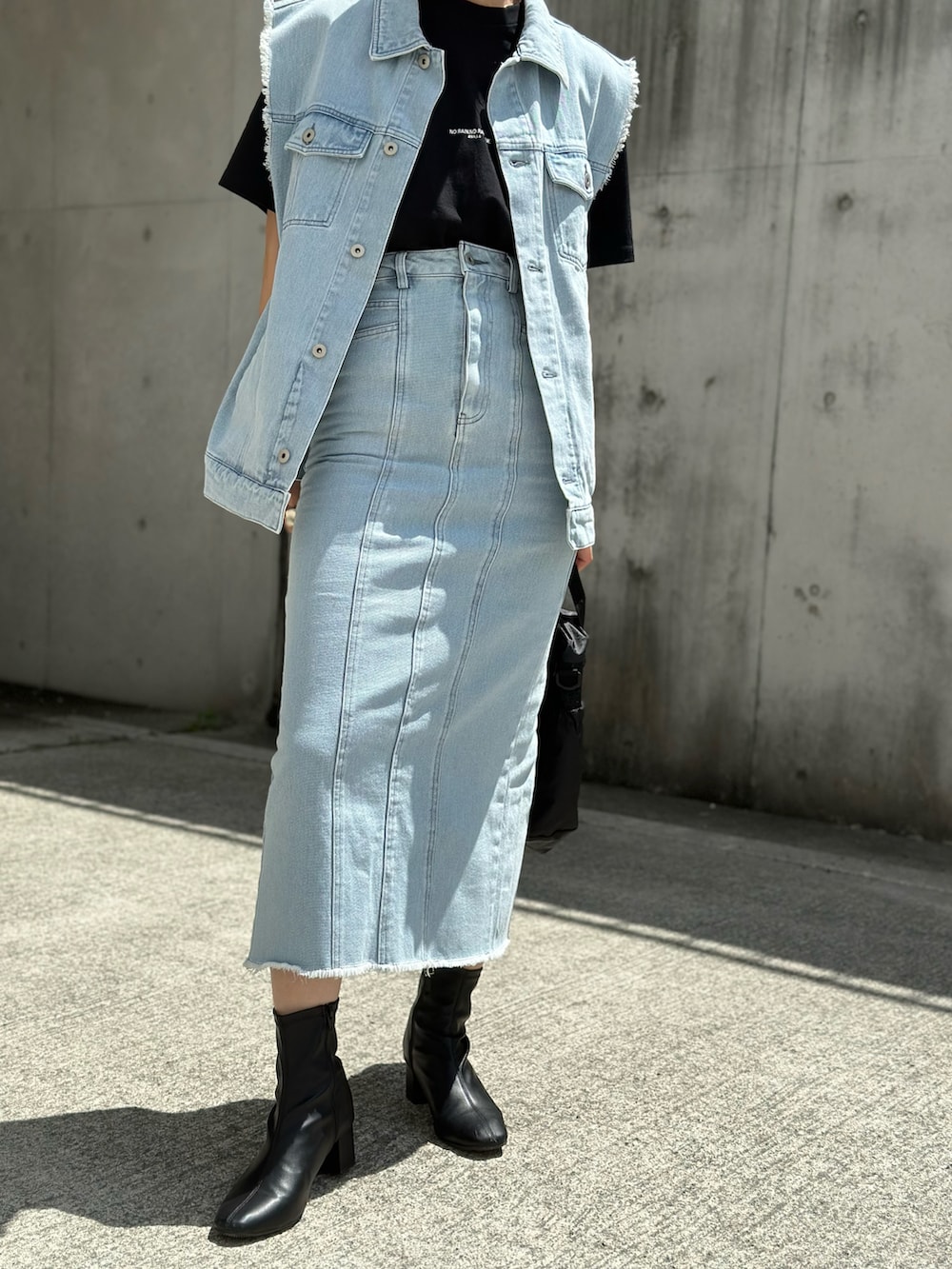 ブルー系のベスト、ブルー系のデニムスカート、ブラック系のTシャツ/カットソーを着用したレディースの春コーディネートの3枚目の写真