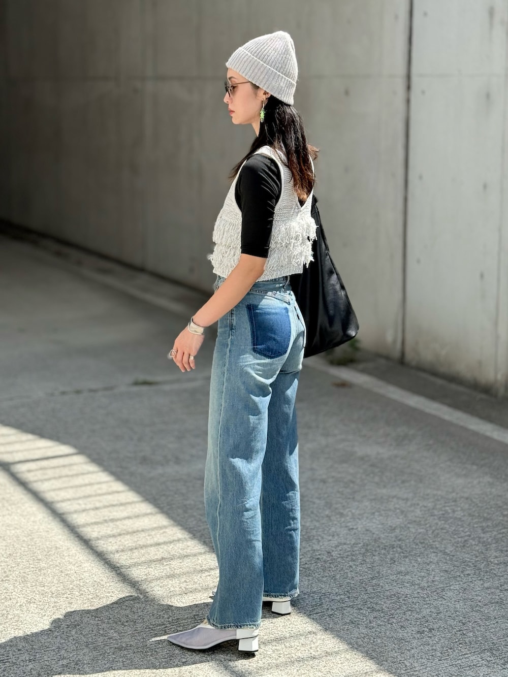 グレー系のベスト、ブラック系のトートバッグ、ブルー系のデニムパンツを着用したレディースの秋コーディネートの3枚目の写真