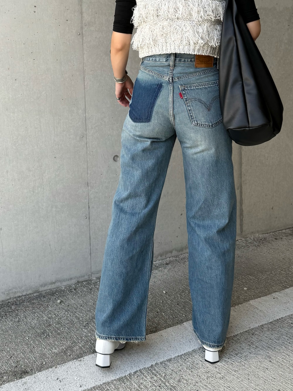 グレー系のベスト、ブラック系のトートバッグ、ブルー系のデニムパンツを着用したレディースの秋コーディネートの5枚目の写真