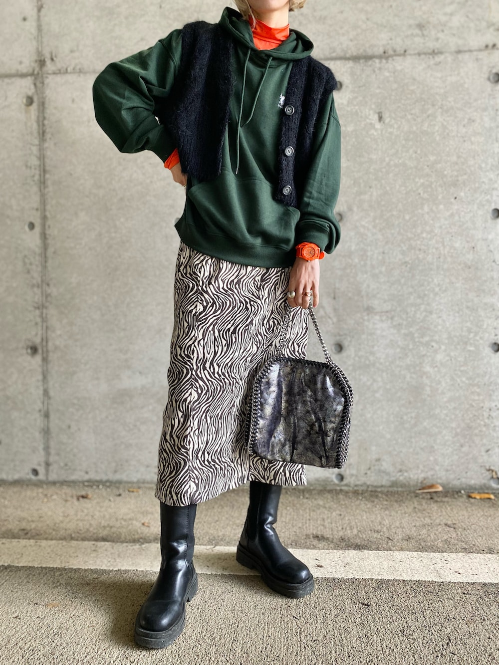 グリーン系のパーカー、ブラック系のベスト、オレンジ系のTシャツ/カットソーを着用したレディースの冬コーディネートの3枚目の写真