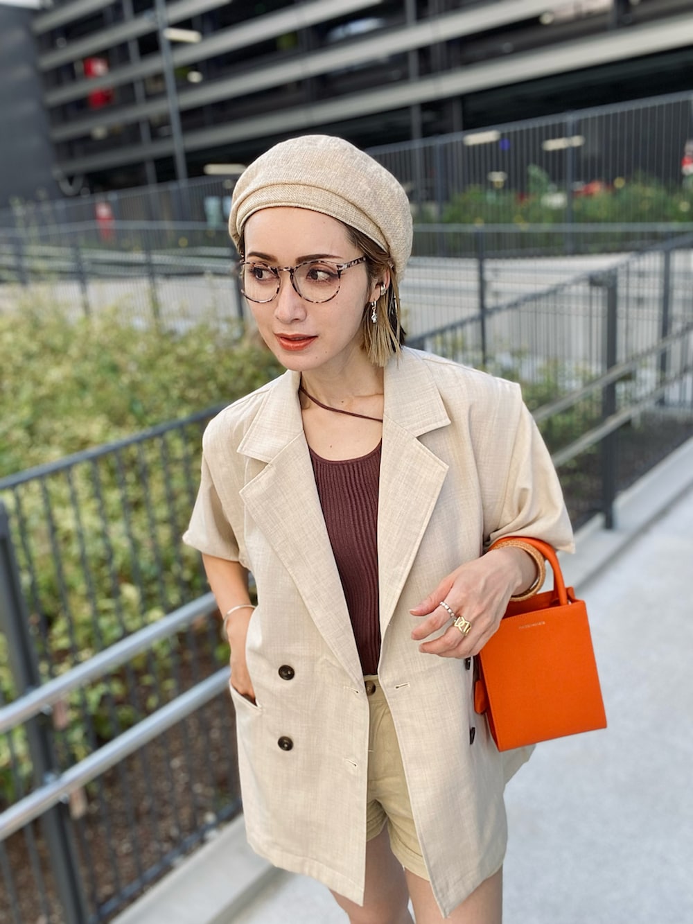 ホワイト系のベスト、ブラウン系のタンクトップ、オレンジ系のトートバッグを着用したレディースの夏コーディネートの2枚目の写真