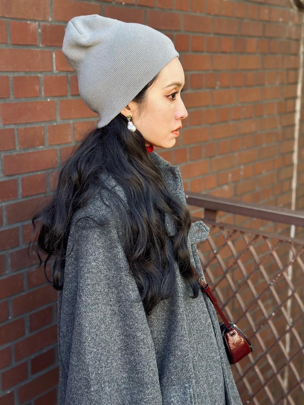 グレー系のステンカラーコート、レッド系のニット/セーター、レッド系のショルダーバッグを着用したレディースの冬コーディネートの4枚目の写真