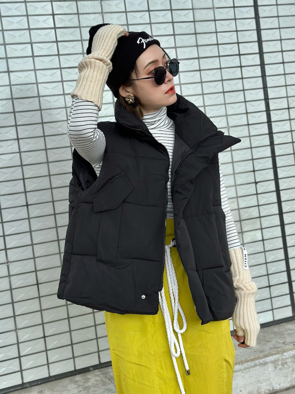ブラック系のダウンベスト、イエロー系のスカート、ホワイト系のスニーカーを着用したレディースの冬コーディネートの4枚目の写真