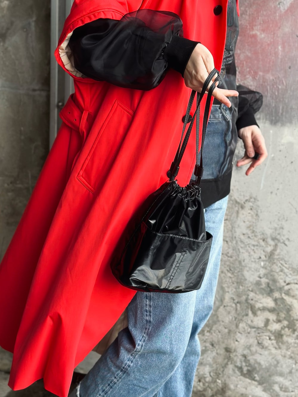 レッド系のトレンチコート、ブラック系のハンドバッグ、ブラック系のTシャツ/カットソーを着用したレディースの春コーディネートの4枚目の写真