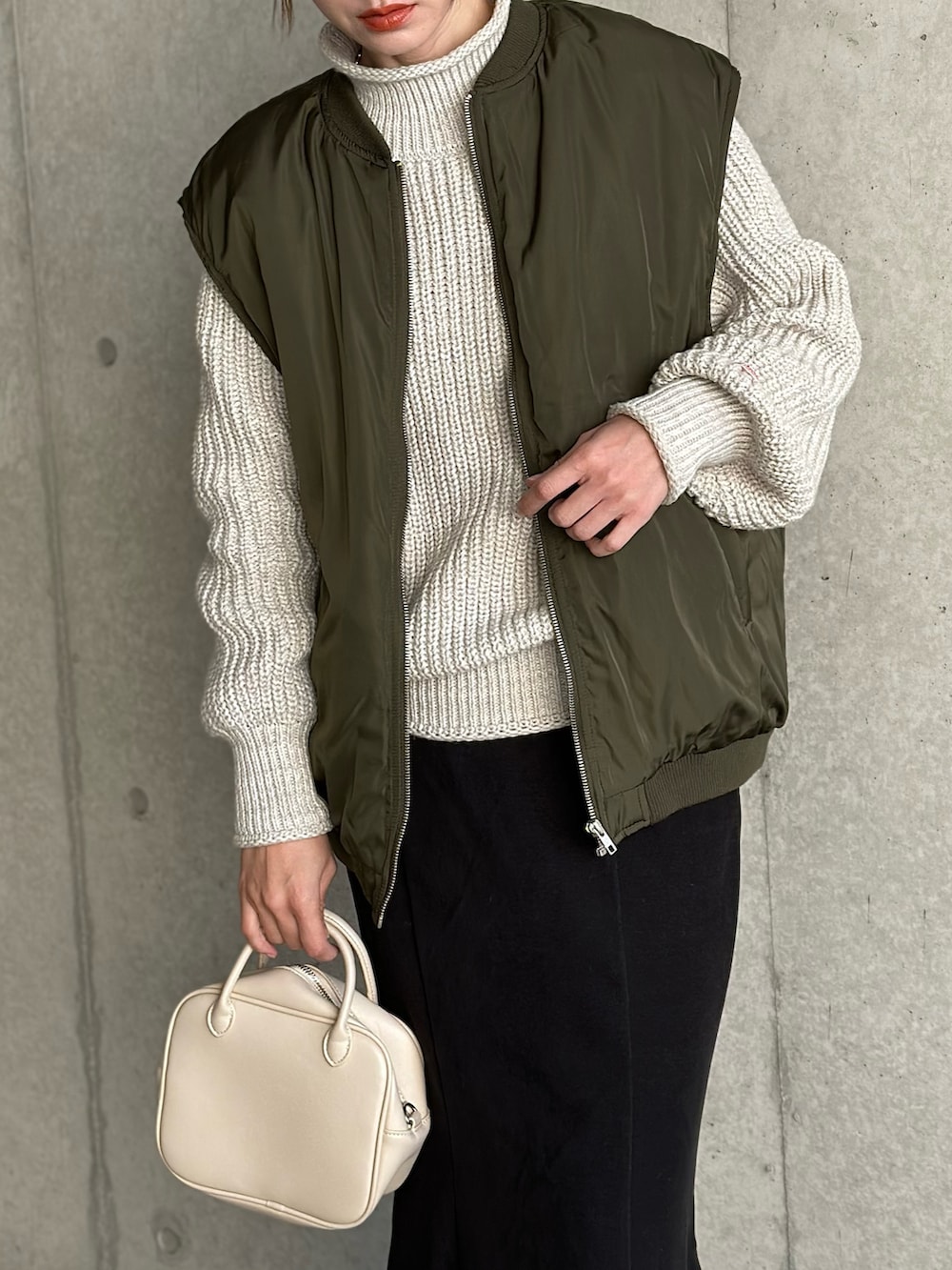 グリーン系のダウンベスト、ベージュ系のニット/セーター、ブラック系のスカートを着用したレディースの冬コーディネートの3枚目の写真