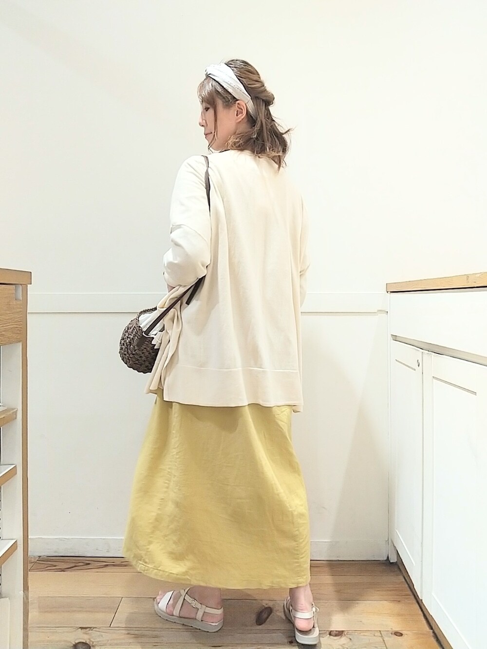 イエロー系のワンピース、ベージュ系のカーディガン/ボレロ、ブラウン系のショルダーバッグを着用したレディースの春コーディネートの2枚目の写真