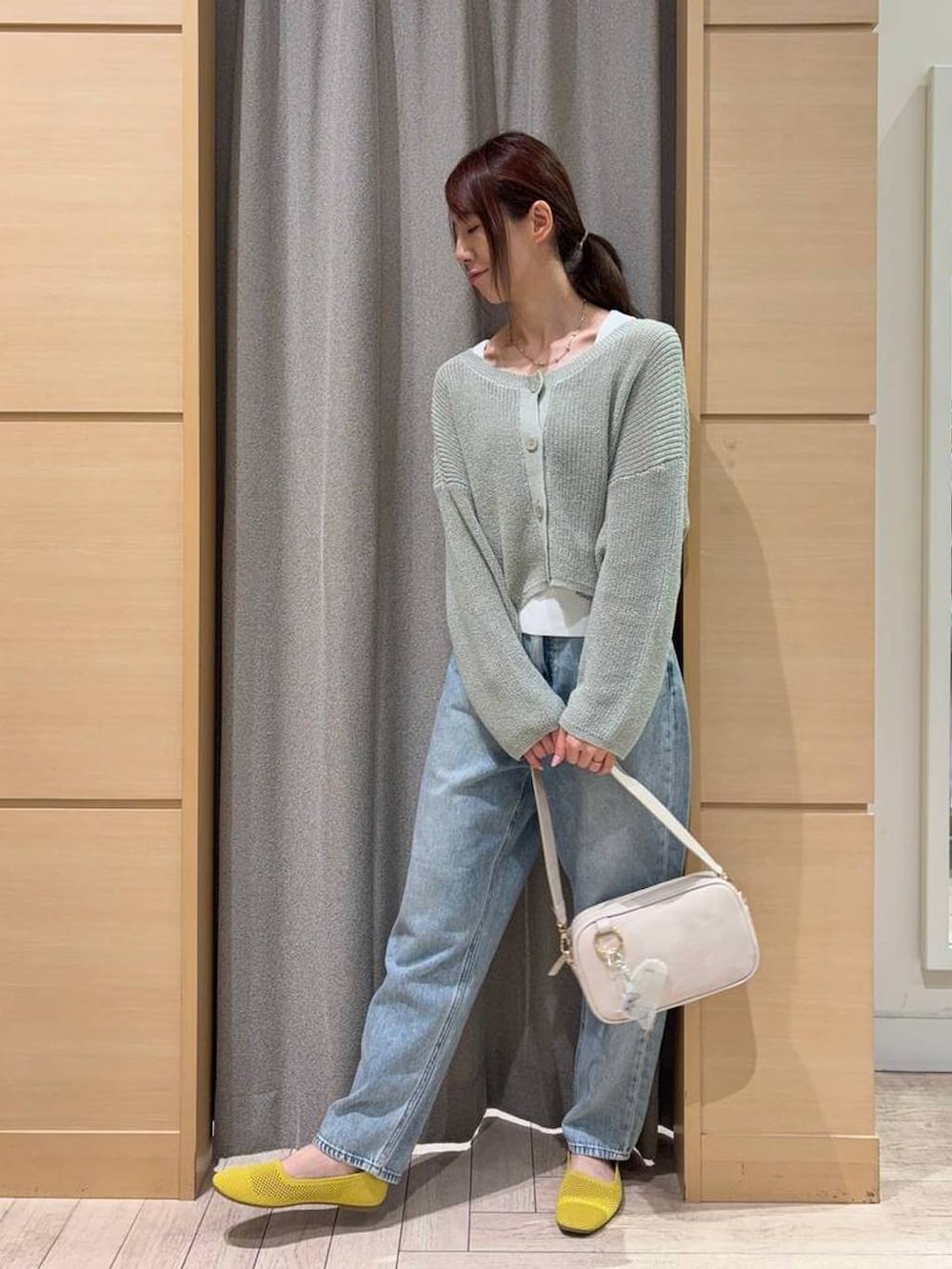 ブルー系のデニムパンツ、ベージュ系のショルダーバッグ、イエロー系のパンプスを着用したレディースの春コーディネートの3枚目の写真